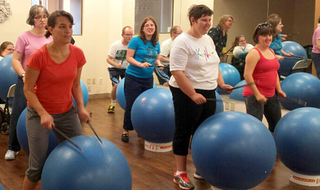 A group of people standing with exercise balls and playing them like a drum.
